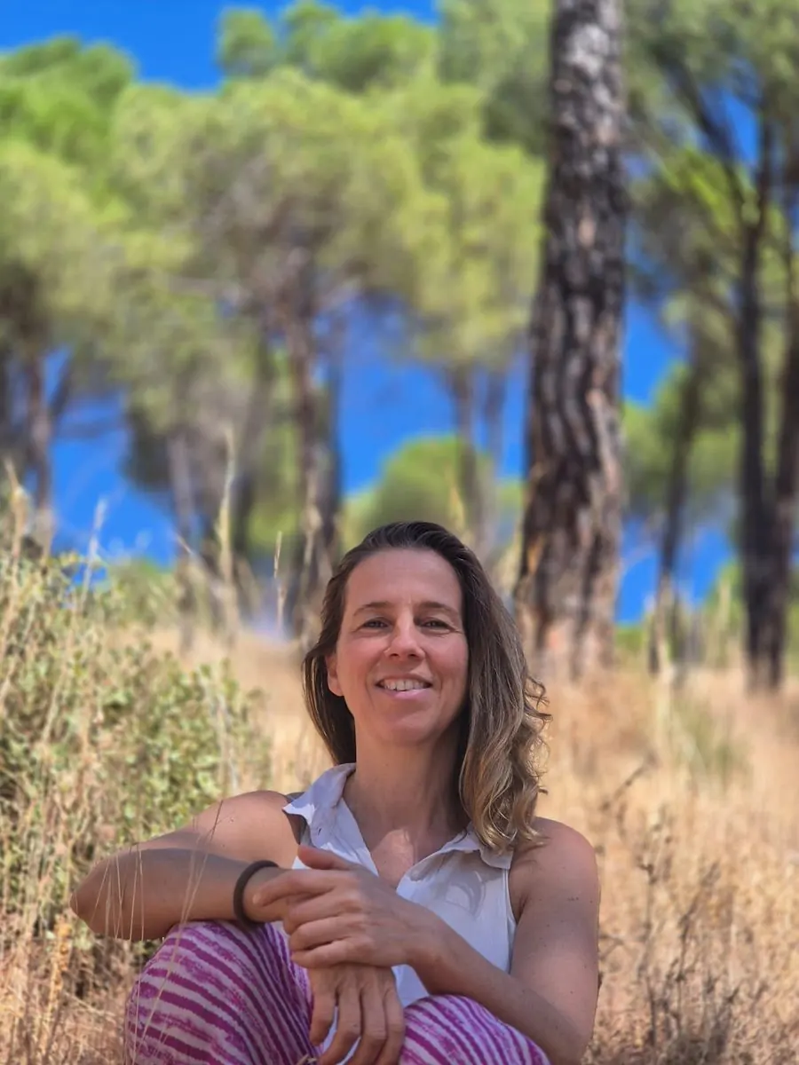 Alicia de la Villa sentada entre pinos, en el campo, con luz de verano