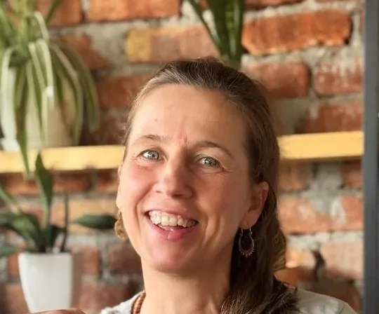 Retrato de Alicia de la Villa sonriendo, en un espacio con plantas y pared de ladrillo